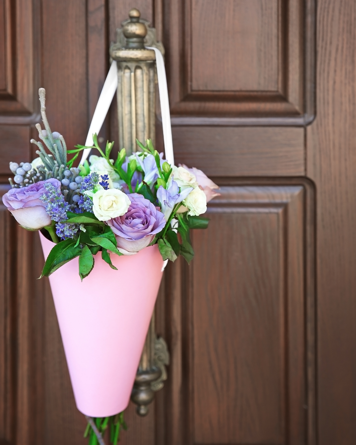 Floral arrangement in a pink cone-shaped container hanging on a wooden door.